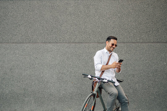 Smiling man on bicycle using smartphone outdoors