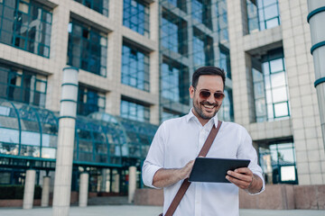 Smiling businessman using digital tablet outside modern office building