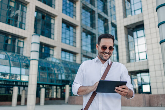 Smiling businessman using digital tablet outside modern office building