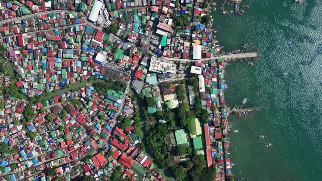 Top‑view rotating aerial of Mariveles town port in Bataan, capturing the dense coastal settlement, colorful rooftops, and busy harbor extending into the calm blue sea.