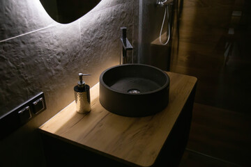Stylish stone sink in a wooden countertop against the background of a mirror with diode lighting...