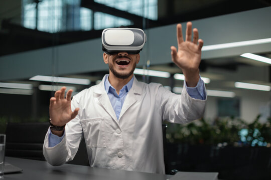 A young middle eastern doctor wearing VR glasses is joyfully interacting with virtual elements in a bright clinic. The modern setting highlights the integration of technology in healthcare.