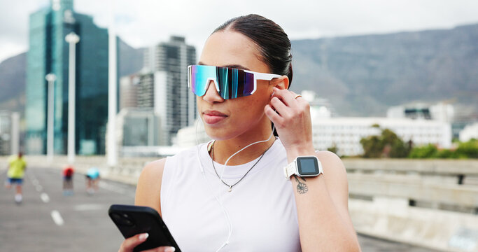 Woman, runner and phone with earphones in city, bridge and audio subscription for training. Person, smartphone and sunglasses with mobile app, listen and streaming music with fitness in urban street