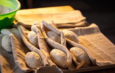Raw bread dough rolls resting on linen cloth for proofing preparation of baking artisanal loaves organic flour seeds green bowl background warm light bakery kitchen setting