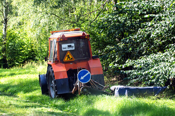 A special tractor with a mower for mowing grass on the side of the road against the background of a forest, industry. Copy space for text
