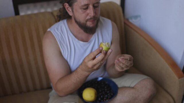 Bearded man eating fresh yellow apple at home