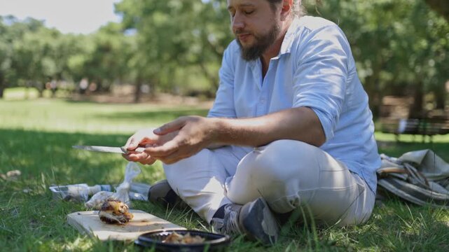 Man enjoying picnic slicing roasted chicken in park