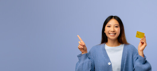 A young woman is smiling happily while holding a yellow card in her right hand and pointing at it...
