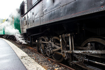 Close-up of a vintage steam locomotive releasing steam, showing detailed mechanical parts and weathered metal.