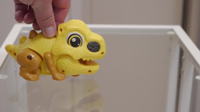 A hollow plastic toy dinosaur is pushed along a smooth glass surface. The motion creates a grating scrape and scratch.