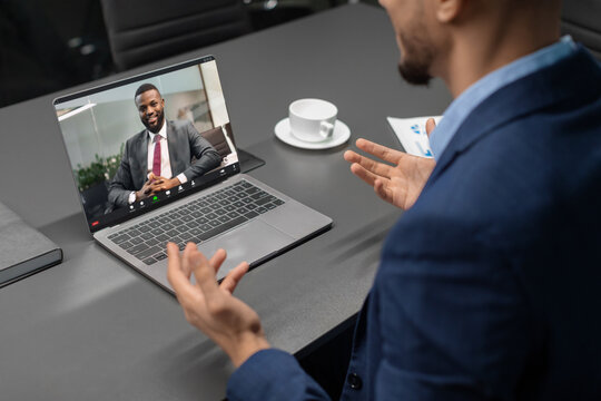 A businessman gestures while having a video conference with an African American CEO. They discuss business strategies using modern technology, both engaged in meaningful conversation.