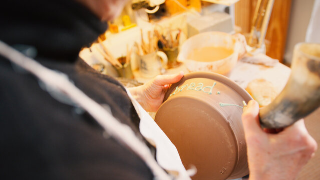 Close Up Of Male Potter Putting Lettering Onto Bread Bowl In Ceramics Studio - Powered by Adobe