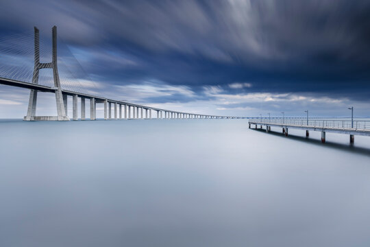 Pont Vasco da Gama sous ciel dramatique &ndash; minimalisme oc&eacute;anique en longue exposition