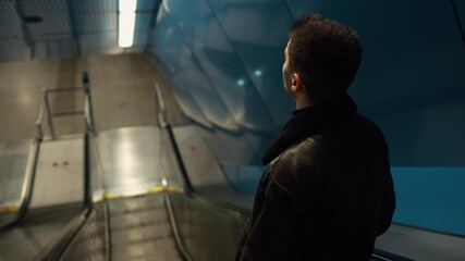 A young man stands on an escalator in a dim urban environment, creating a cinematic, modern scene that reflects daily commute, city life, and contemporary underground spaces.