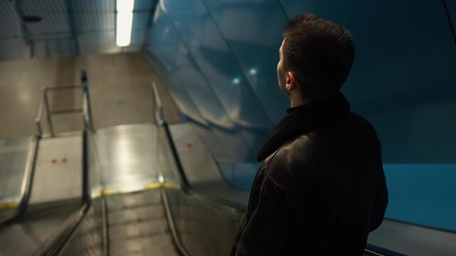 A young man stands on an escalator in a dim urban environment, creating a cinematic, modern scene that reflects daily commute, city life, and contemporary underground spaces.