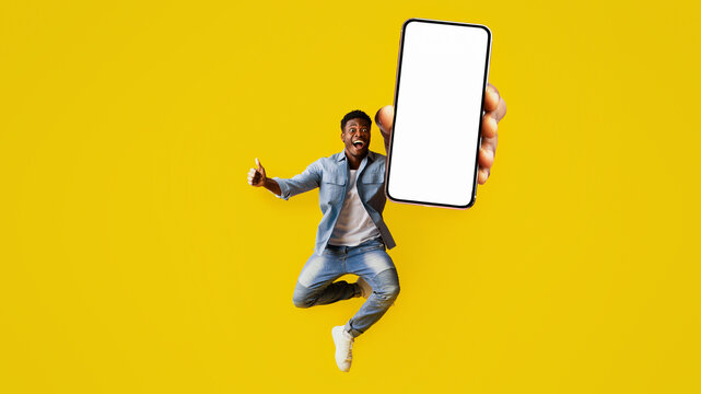 A young man expresses excitement by jumping into the air. He holds a smartphone up with a blank screen in his hand. The vibrant yellow background adds to the lively atmosphere.