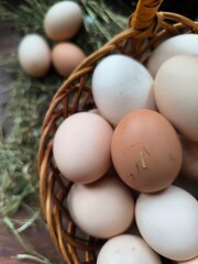 Fresh chicken eggs in a wicker basket on hay, wooden background