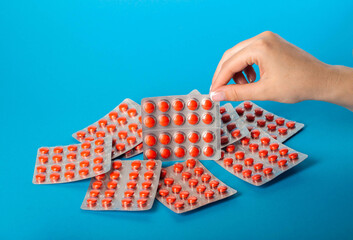 Blister pack with red pills in a female hand on a blue background. Concept of statin pills for lowering cholesterol in the blood. Copy space for text, bile acid sequestrants