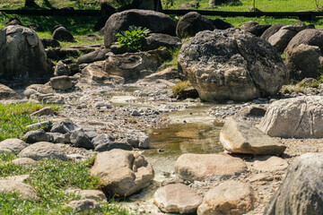 rocky geothermal field or the source area of a hot spring. The scene is dominated by large, weathered granite boulders scattered across a mostly dry streambed. The ground between the rocks is covered 