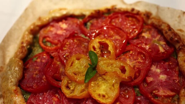 A delicious tomato galette is displayed on parchment paper, showcasing layers of vibrant red and yellow tomatoes atop a flaky crust in a warm kitchen atmosphere.