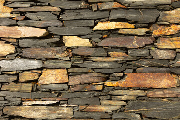 Xisto. A traditional dry-stone wall made of irregular, layered slate pieces. The mix of dark greys, browns, and rusty tones highlights natural textures and the craftsmanship typical