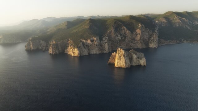 Aerial view of rugged cliffs meet the tranquil sea, illuminated by the golden light of sunrise near Capo Pecora, Sardinia, Italy.