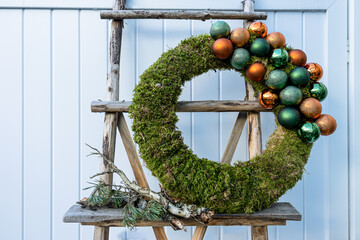 Moss wreath with Christmas baubles standing on rustic ladder
