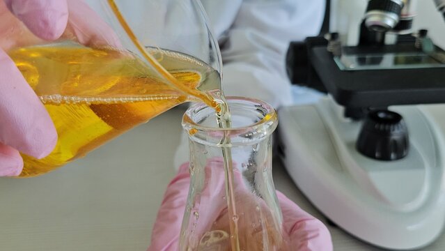 Scientist chemist pouring liquid into flask with motor oil in laboratory closeup. Quality control of petroleum products concept - Powered by Adobe