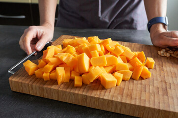 A woman dicing a pumpkin on a wooden board. Selective focus. Shallow depth of field.