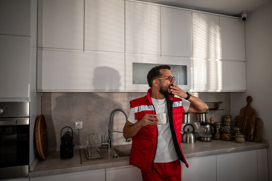 Paramedic man yawning while having coffee in kitchen