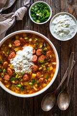 Potato soup with sausage and yogurt on wooden table. Top view
