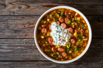 Potato soup with sausage and yogurt on wooden table. Top view