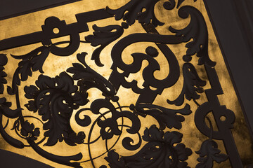 Naklejka premium Intricate black iron scrollwork silhouetted against a rich gold background,