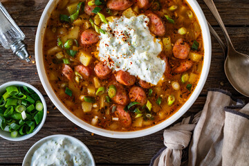 Potato soup with sausage and yogurt on wooden table. Top view