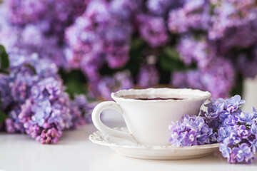 The concept of home comfort and drinks. A cup of tea or coffee on the table. In the background is a large purple bouquet of lilacs.