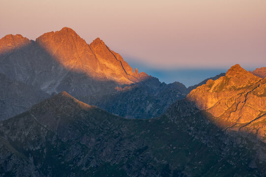 Aerial view of the rugged, sun-kissed peaks of Jahnaci stit pierce the soft pastel sky, casting long shadows across the Slovakian landscape, Vysoke Tatry, Presov Region, Slovakia.