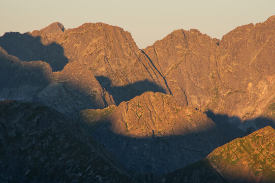 Aerial view of Jahnaci stit peak bathed in the warm glow of the setting sun, casting long shadows across the rugged terrain, Vysoke Tatry, Presov Region, Slovakia.