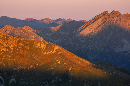 Aerial view of sunlight casting warm hues across the rugged peaks and valleys of Jahnaci stit peak, creating a breathtaking tapestry of light and shadow, Vysoke Tatry, Presov Region, Slovakia.