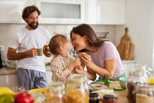 A joyful family spends time together in their modern kitchen. The child shares a sweet moment with a parent while another adult enjoys a drink nearby, creating a warm atmosphere of love.