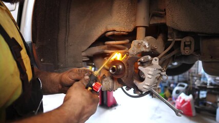 Skilled mechanic using a torch to heat brake components, showcasing the intricate process of automotive repair in a well-equipped garage environment with tools and parts visible