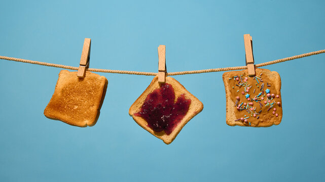 Toast slices with toppings hanging on rope against blue background. Concept of breakfast campaigns, cafe branding, snack packaging, product marketing and pop-culture visuals.