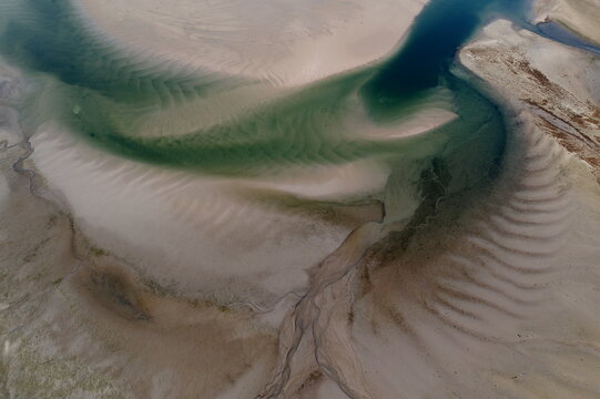 Aerial view of swirling turquoise waters carve intricate patterns through the beige sands, creating a mesmerizing dance of color and texture, Findhorn, Scotland, United Kingdom.
