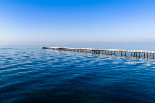 Long pier stretching into calm blue water under a clear sky. Minimalistic seascape with peaceful waves and clean horizon. - Powered by Adobe