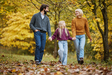 A family takes a leisurely walk in a beautiful park during autumn, enjoying each other's company amidst falling leaves and striking colors.