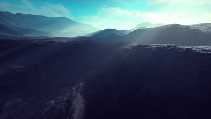 Morning light illuminates a breathtaking mountain range, with mist swirling through the valleys. The vibrant blue sky contrasts with the rugged terrain, creating a serene atmosphere.