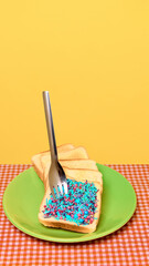 Toast slice with bright sprinkles pierced by fork on green plate and yellow background. Concept of snack branding, dessert menu photos, bakery promos, fun food stories and lifestyle content.