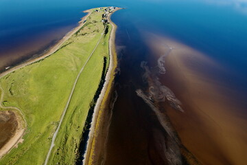 Aerial view of emerald green fields meet the dark waters, divided by a golden sandy shore leading to a distant point, Dornoch, United Kingdom.