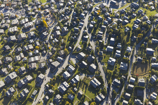 Aerial view of rooftops basking under the sun, nestled among winding roads and scattered trees, creating a textured tapestry of urban life, Val de Bagnes, Valais, Switzerland.