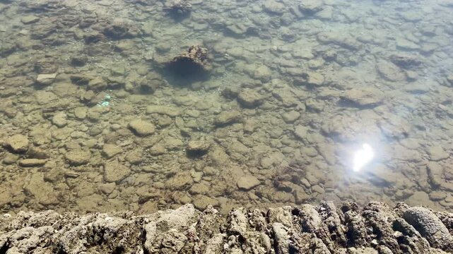 Sunlight sparkles on crystal clear tidal water beside the rough stone wall of the historic fish corrales in Chipiona on a calm Atlantic morning