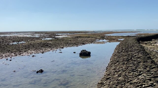 a Wide shot of the Chipiona stone fish corrales curving across the tidal flats at low tide under a clear blue Atlantic sky